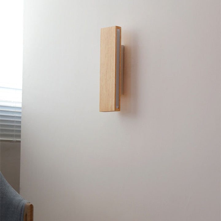 Side view of the unlit wooden wall lamp in a vertical position, mounted on a white wall near a window. 2