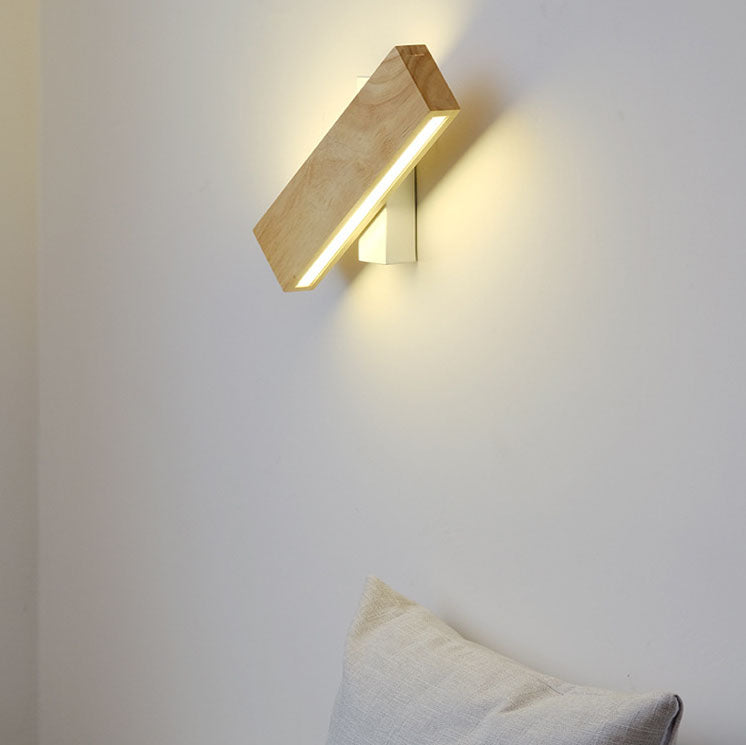 Wooden rotating wall lamp turned diagonally on a white wall, glowing warmly, with a light cushion below. 1