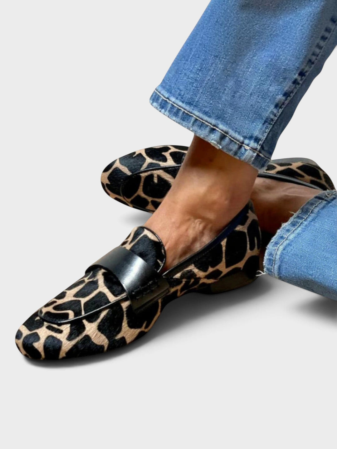 Nogi w jeansach z podwiniętą nogawką, ze skrzyżowanymi stopami w loaferach w czarno-beżowy wzór z czarnym skórzanym paskiem. 1