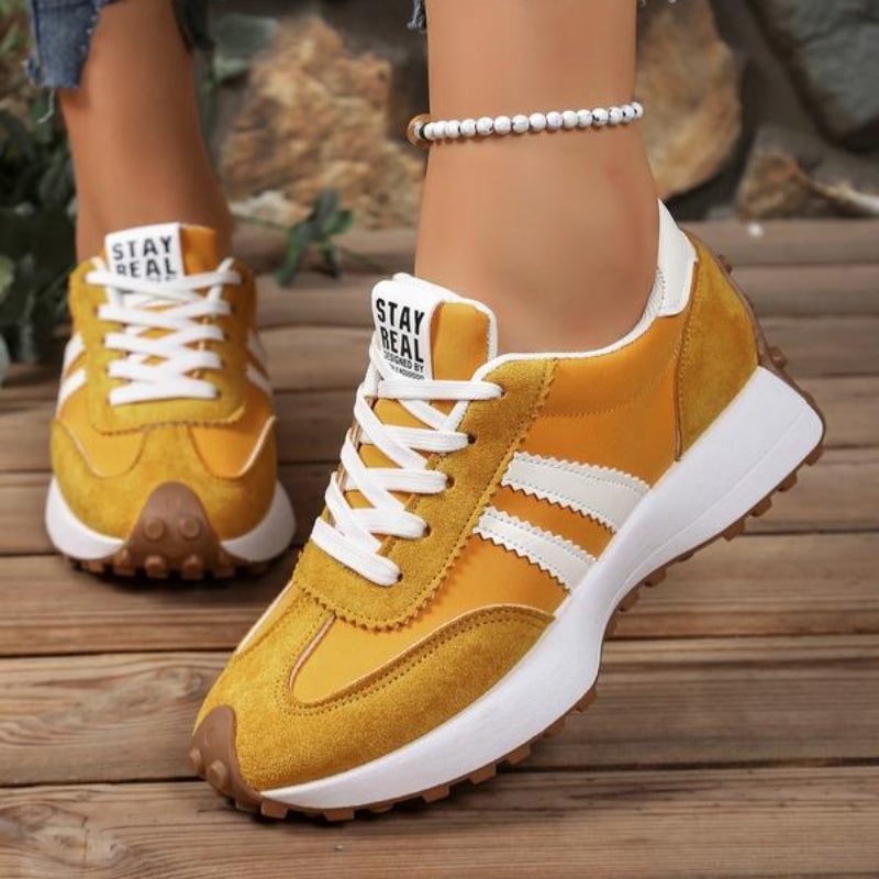 Żółte sneakersy z białymi paskami i sznurowadłami na stopach modelki, ustawione na drewnianych deskach 6