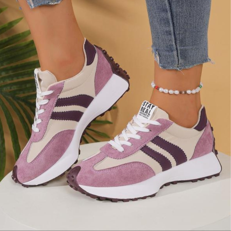 Różowo-beżowe sneakersy z fioletowymi paskami na nogach modelki, widok z boku na grubej białej platformie 12
