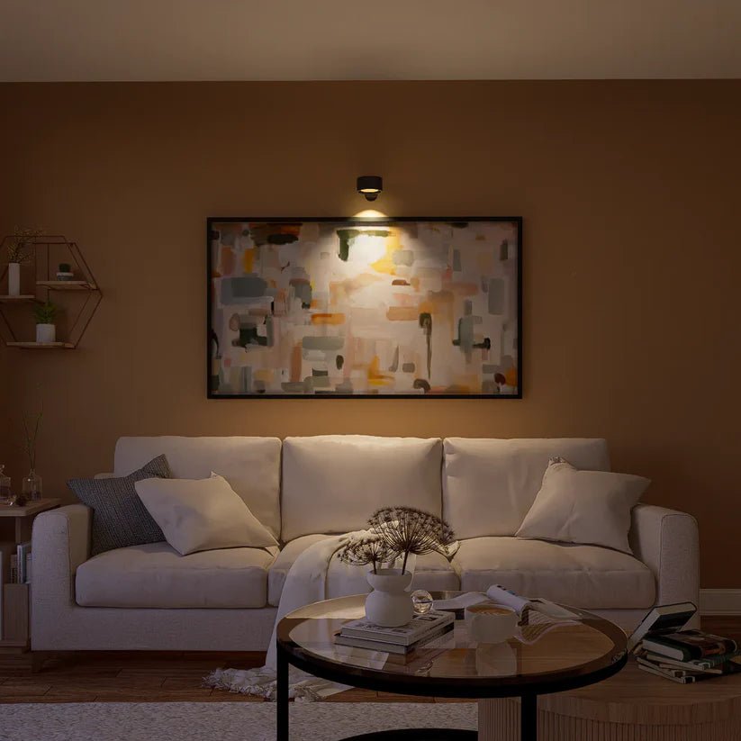 Czarna lampa ścienna podświetla obraz abstrakcyjny nad jasną sofą w salonie wieczorem. 8
