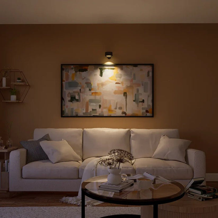 Czarna lampa ścienna podświetla obraz abstrakcyjny nad jasną sofą w salonie wieczorem. 8