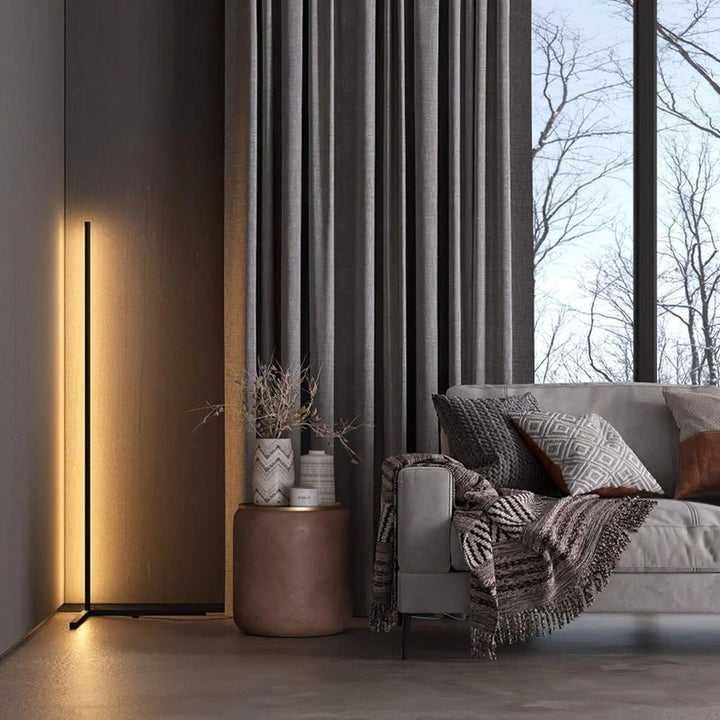 Lampa z ciepłą poświatą w salonie, obok okrągłego stolika z wazonami i szarej sofy z kocem 3
