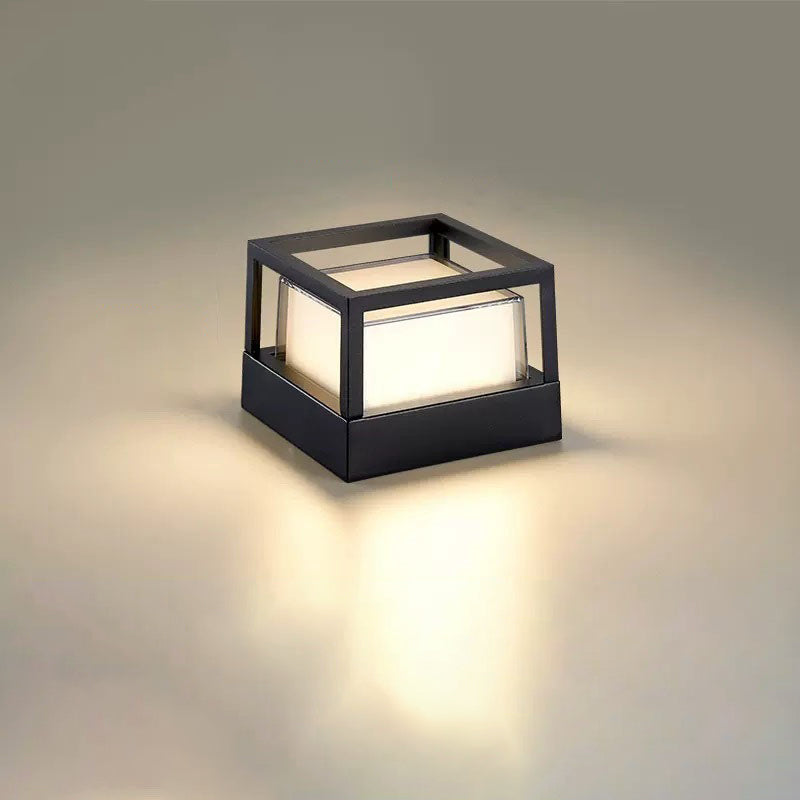 Kwadratowa lampa z otwartą czarną ramą bez daszka, widoczny mleczny klosz i ciepłe światło na jasnym tle. 11