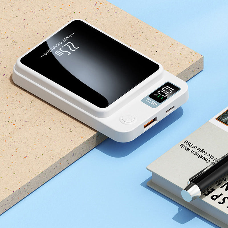 Biały powerbank leżący na blacie, widać wyświetlacz, przycisk, port USB i złącze USB-C, obok książka i długopis. 6