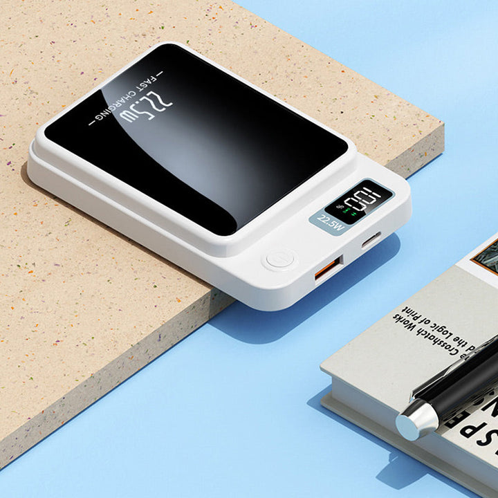 Biały powerbank leżący na blacie, widać wyświetlacz, przycisk, port USB i złącze USB-C, obok książka i długopis. 6