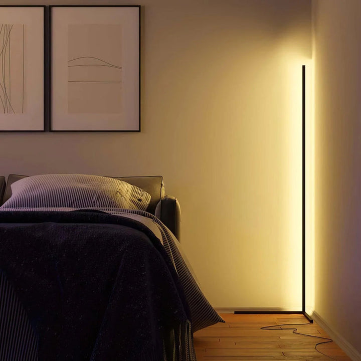 Narożna lampa rozświetlająca ścianę ciepłym światłem w sypialni, obok łóżka i dwóch obrazów w ramach 4