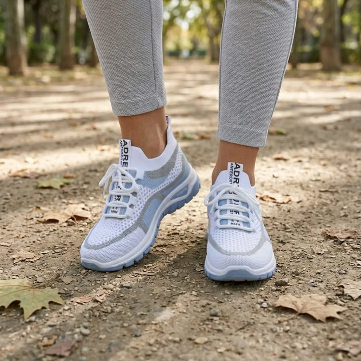 Białe sneakersy z niebieską podeszwą noszone na stopach, spacer ścieżką w parku wśród jesiennych liści. 2