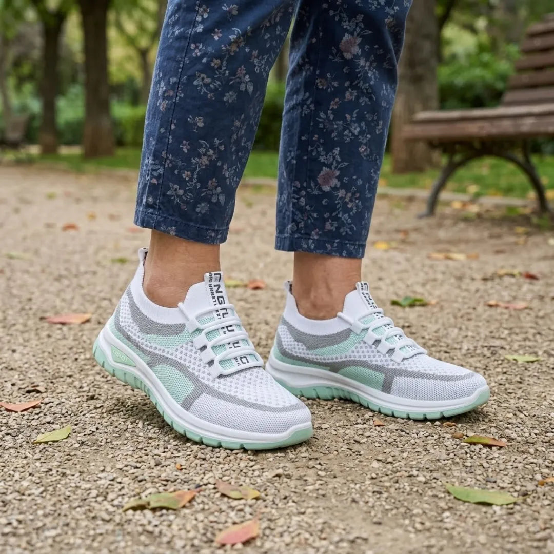 Białe sneakersy z miętowozieloną podeszwą noszone z kwiecistymi niebieskimi spodniami, na żwirowej ścieżce w parku. 11
