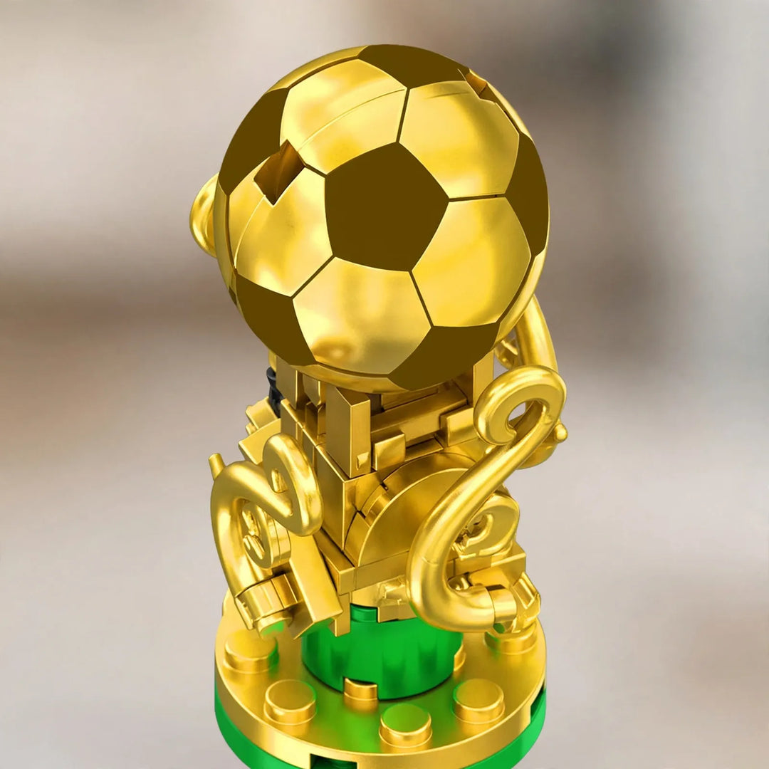 Zbliżenie na złote klockowe trofeum z piłką na szczycie, ozdobnymi uchwytami i zieloną podstawą 3