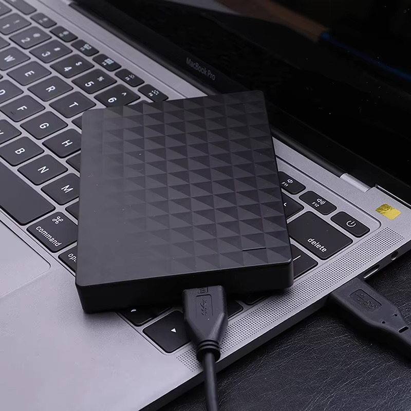 Dysk leżący na klawiaturze laptopa, połączony czarnym kablem USB 3.0 z komputerem 3