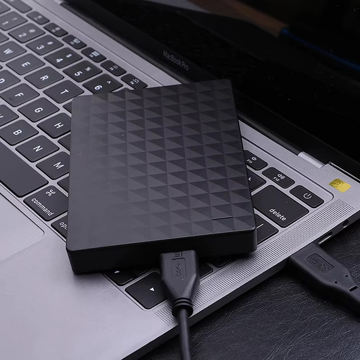 Dysk leżący na klawiaturze laptopa, połączony czarnym kablem USB 3.0 z komputerem 3