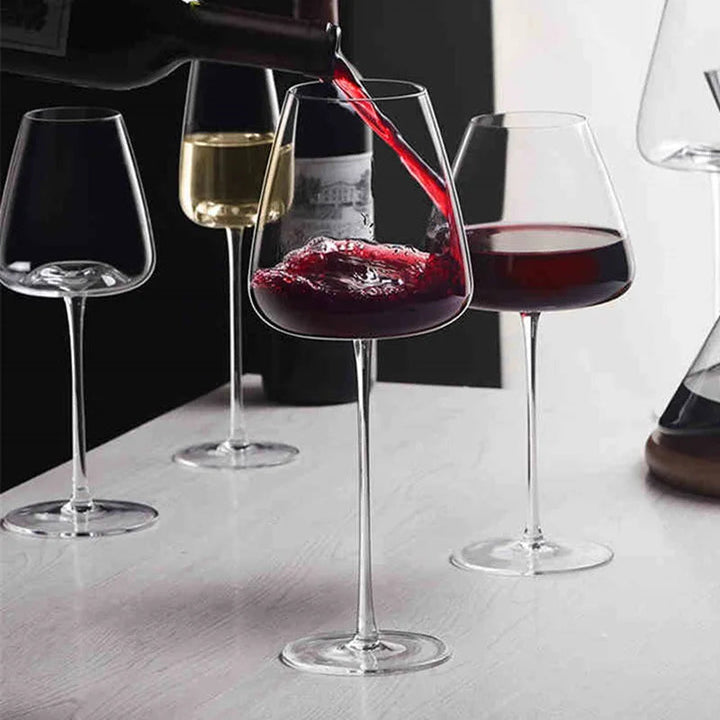 Czerwone wino wlewane z butelki do kieliszka, obok kieliszki z winem białym i czerwonym oraz karafka 2