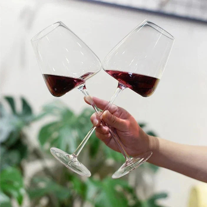 Dłoń trzymająca dwa przechylone kieliszki z czerwonym winem, jakby wznosiła toast, na tle zielonych roślin 7