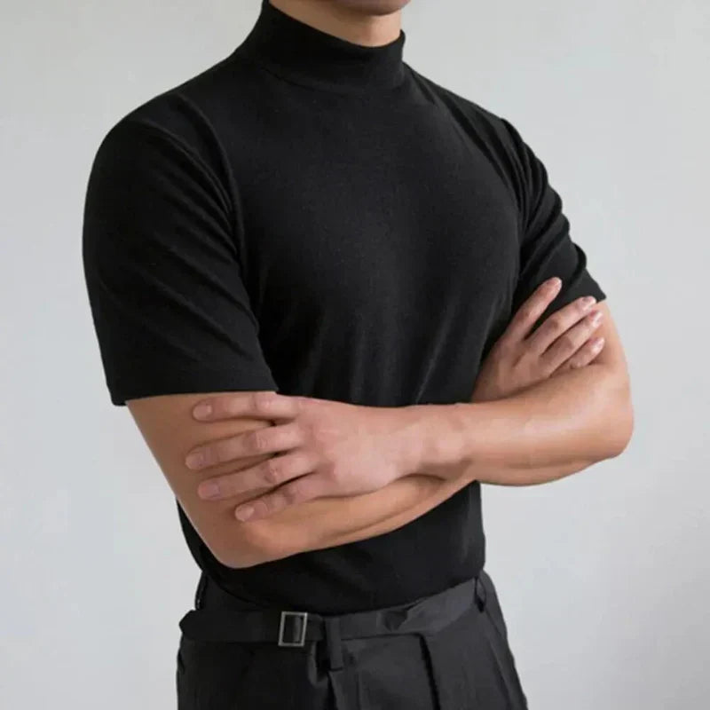Ten sam czarny t-shirt z półgolfem na modelu ze skrzyżowanymi rękami, ujęcie na jasnoszarym tle. 2