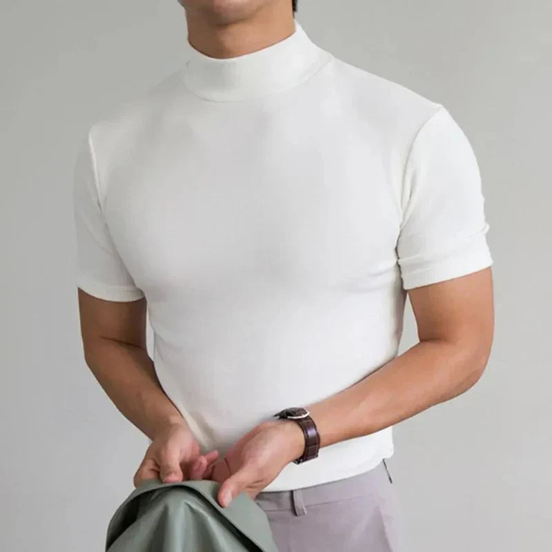 Biały t-shirt z półgolfem na modelu w jasnych spodniach, z zegarkiem na nadgarstku i zieloną kurtką w dłoniach. 4