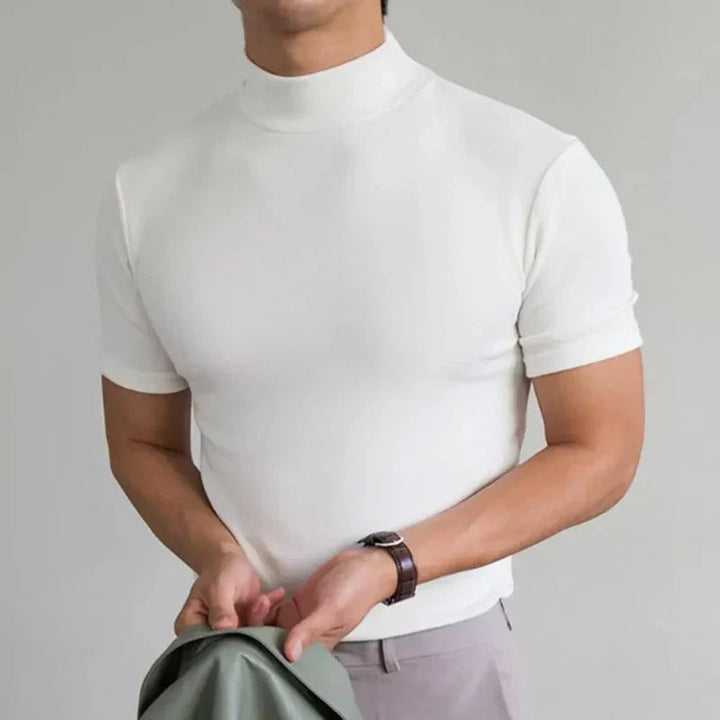 Biały t-shirt z półgolfem na modelu w jasnych spodniach, z zegarkiem na nadgarstku i zieloną kurtką w dłoniach. 4
