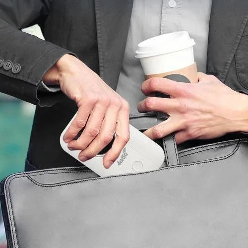 Mężczyzna w marynarce wsuwa mały biały router do szarej torby na dokumenty, w drugiej ręce trzyma kubek kawy 2