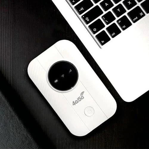 Biały router leżący na ciemnym blacie obok klawiatury laptopa, widok z góry 5