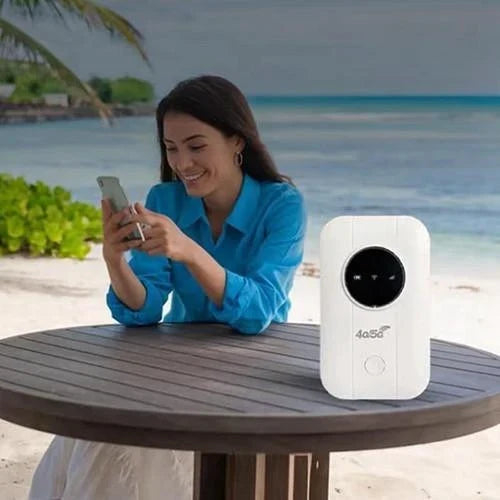 Kobieta w niebieskiej koszuli korzysta ze smartfona przy stoliku na plaży, obok stoi biały router 6