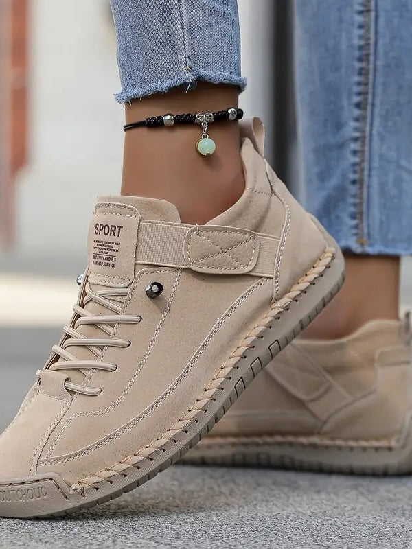 Beżowe zamszowe sneakersy na stopach modelki w dżinsach, z paskiem na podbiciu i bransoletką na kostce 14
