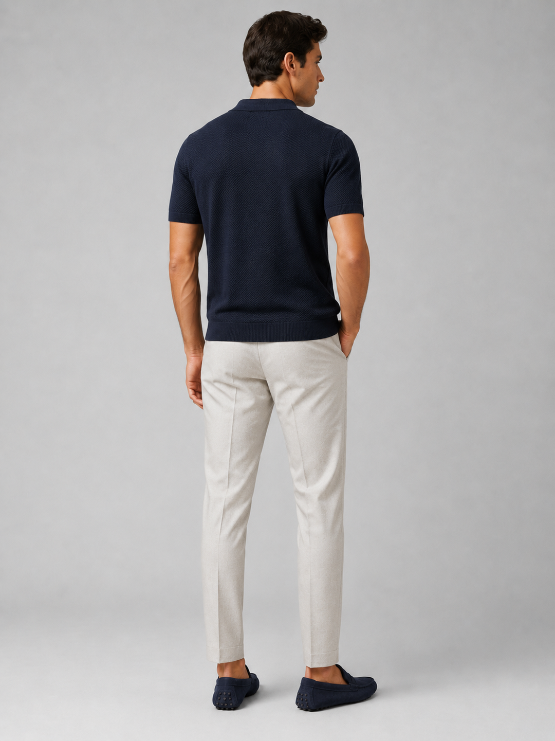 Granatowa koszulka polo widziana od tyłu, model w jasnych spodniach i granatowych mokasynach 38