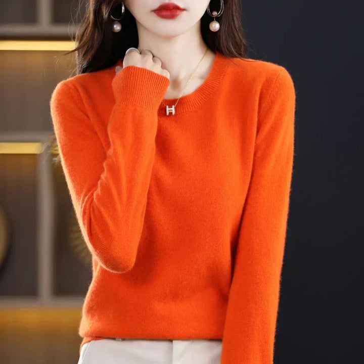 Pomarańczowy sweter z okrągłym dekoltem, modelka przy szyi trzyma dłoń zgiętą w pięść 5