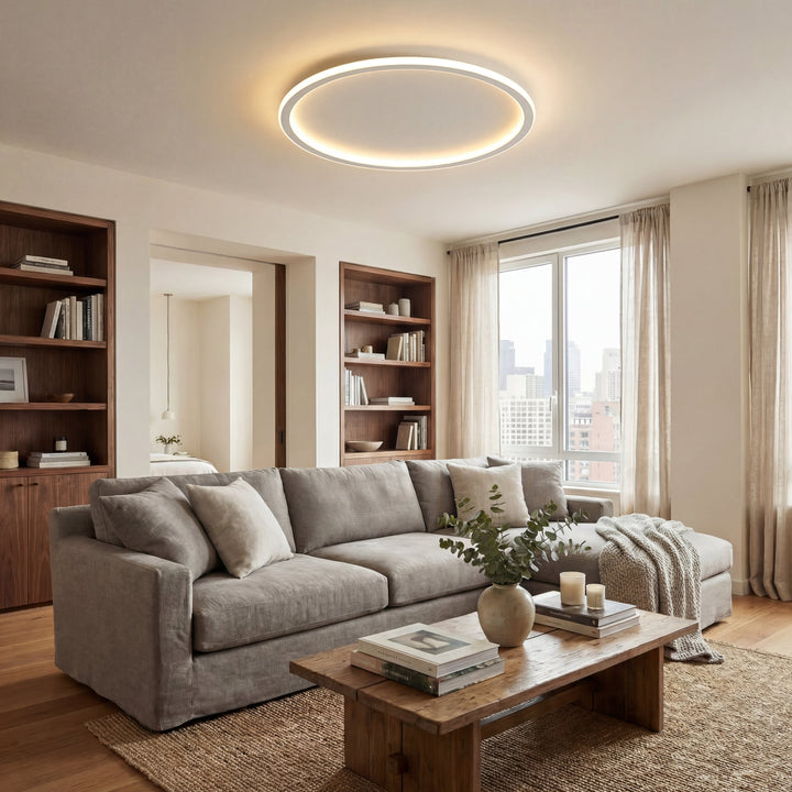 Lampa w kształcie pierścienia nad szarą narożną sofą i drewnianym stolikiem w jasnym salonie z regałami i oknem. 5
