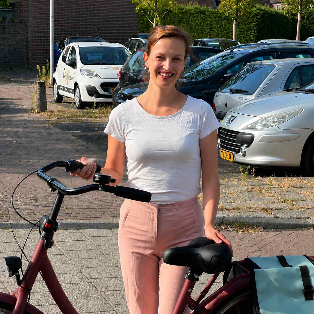 Uśmiechnięta kobieta stoi obok roweru miejskiego z zamontowanym czarnym siodełkiem i niebieskimi sakwami. 7