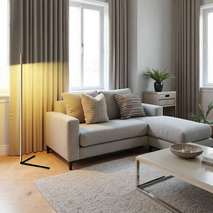 Lampa z ciepłym światłem oświetlająca zasłonę w jasnym salonie z jasną narożną sofą i stolikiem kawowym 10