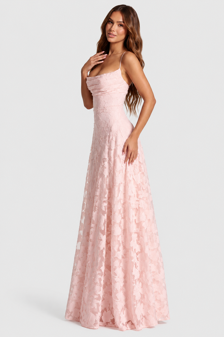 Modelka w jasnoróżowej sukience z kwiatową koronką i drapowanym dekoltem, ujęcie z boku, dłoń przy dekolcie. 1