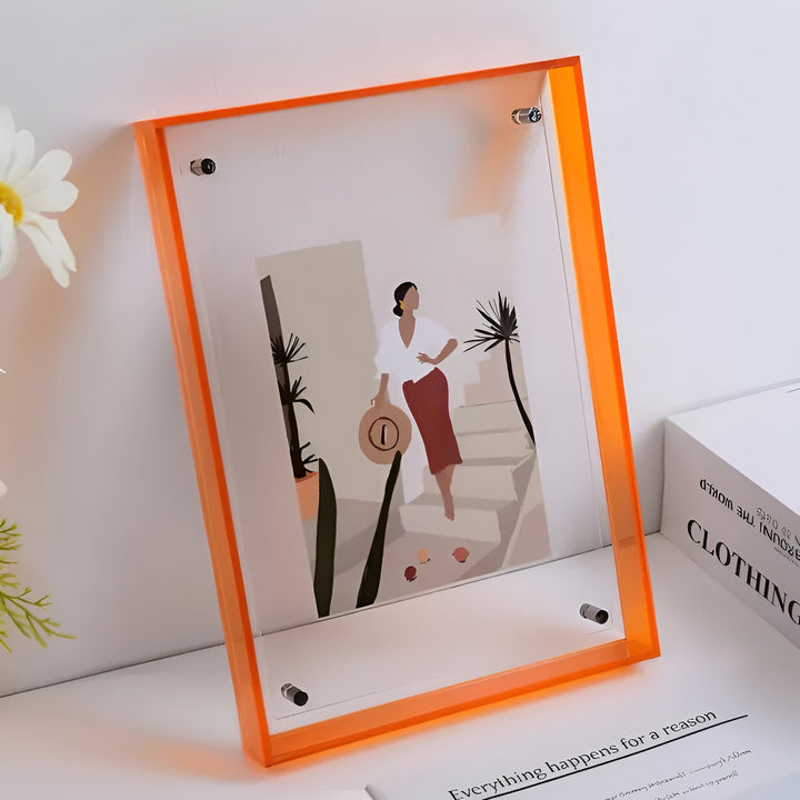 Pomarańczowa ramka akrylowa z bolcami w rogach, w środku ilustracja kobiety w kapeluszu przy palmach, obok kwiat i książka. 10