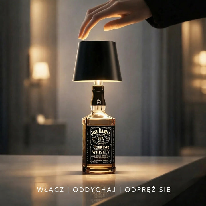 Dłoń zbliża się do czarnego klosza lampy na butelce whisky, by ją dotknąć 6