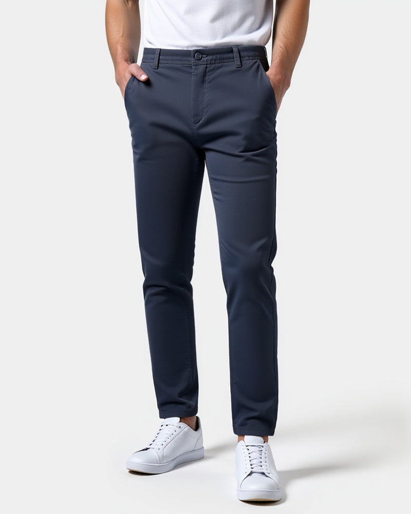 Granatowe chinosy na modelu w białym t-shircie i białych sneakersach, ujęcie z przodu, obie dłonie w kieszeniach. 15