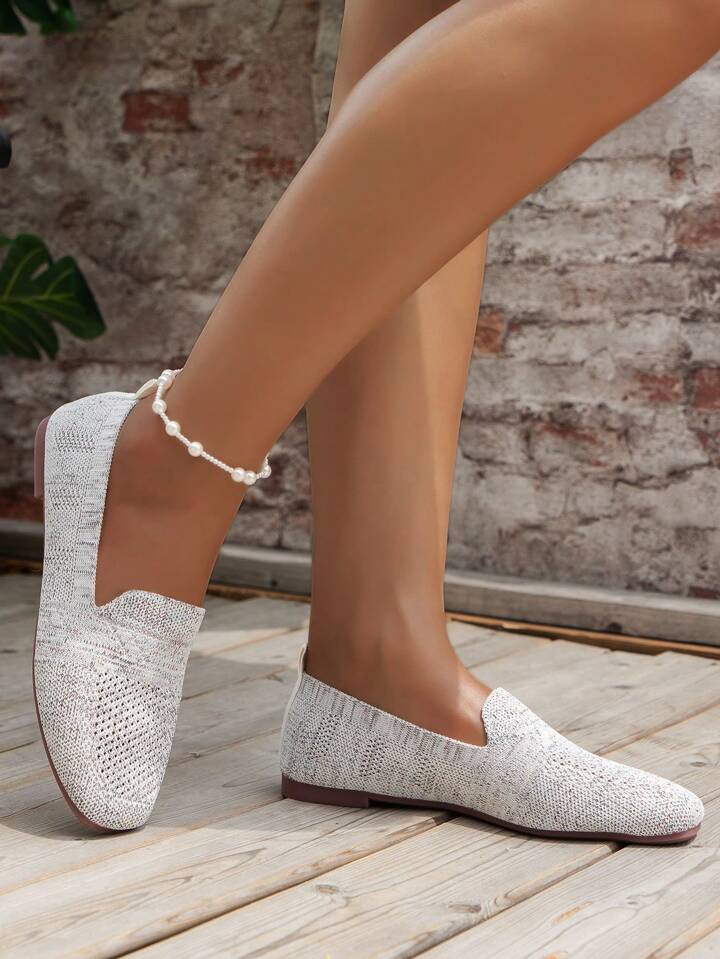 Białoszare dzianinowe buty wsuwane na nogach modelki, widok z boku na tle ceglanej ściany i drewnianej podłogi. 14