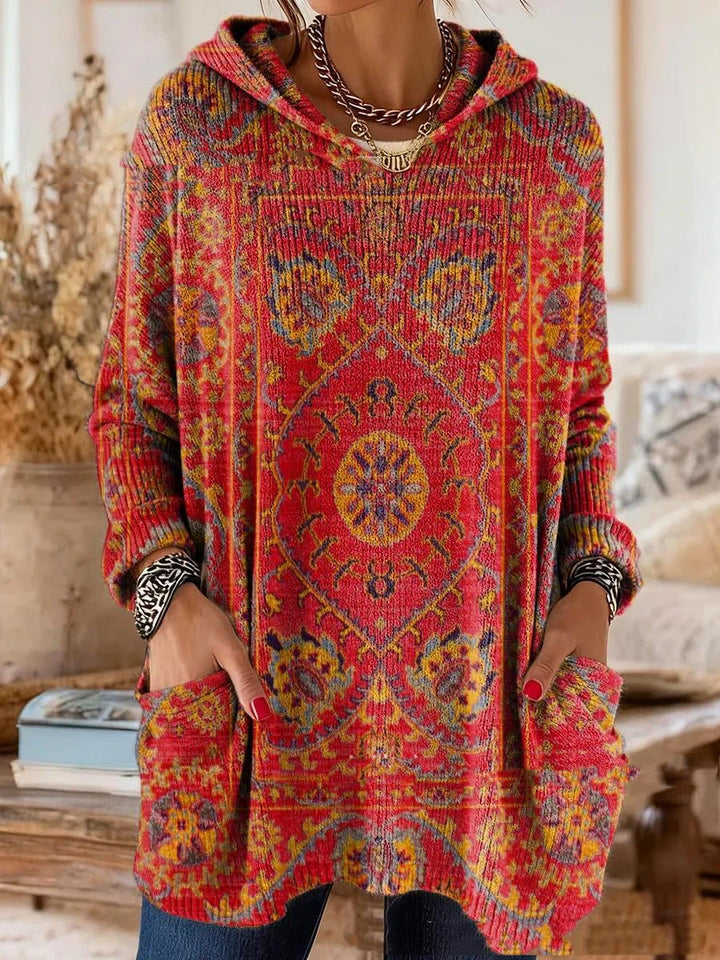 Czerwona tunika z kapturem ze złoto-niebieskim ornamentem orientalnym, widok z przodu na modelce z rękami w kieszeniach. 4
