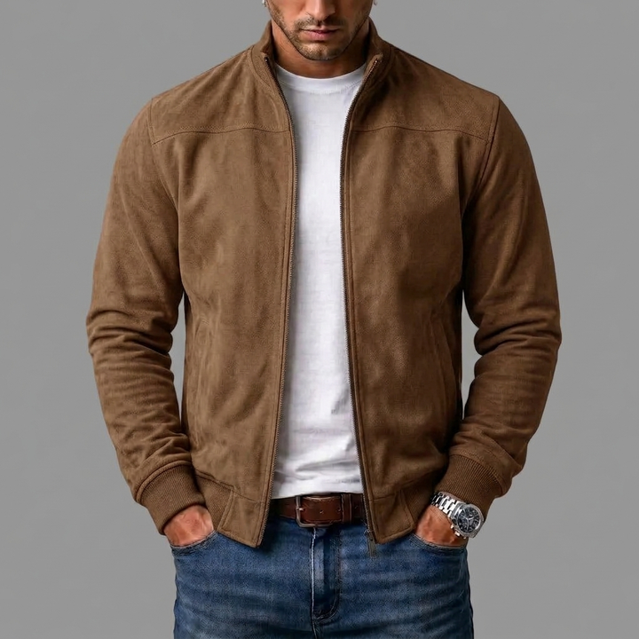 Mężczyzna w brązowej kurtce bomber z imitacji zamszu, rozpiętej na białym t-shircie, z rękami w kieszeniach jeansów. 4