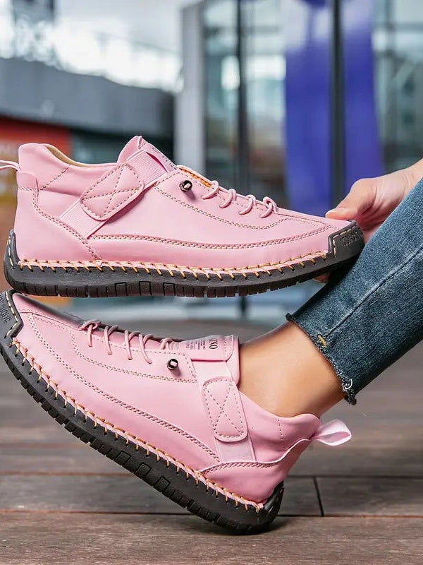 Różowe sneakersy z jasnymi przeszyciami i czarną podeszwą, trzymane i noszone przez modelkę 13