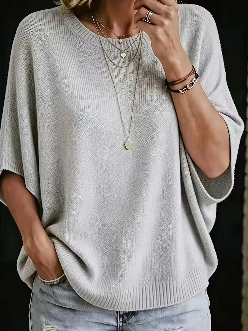 Jasnoszary dzianinowy top z rękawami batwing, zbliżenie z przodu na modelce z kilkoma naszyjnikami i dżinsami. 1