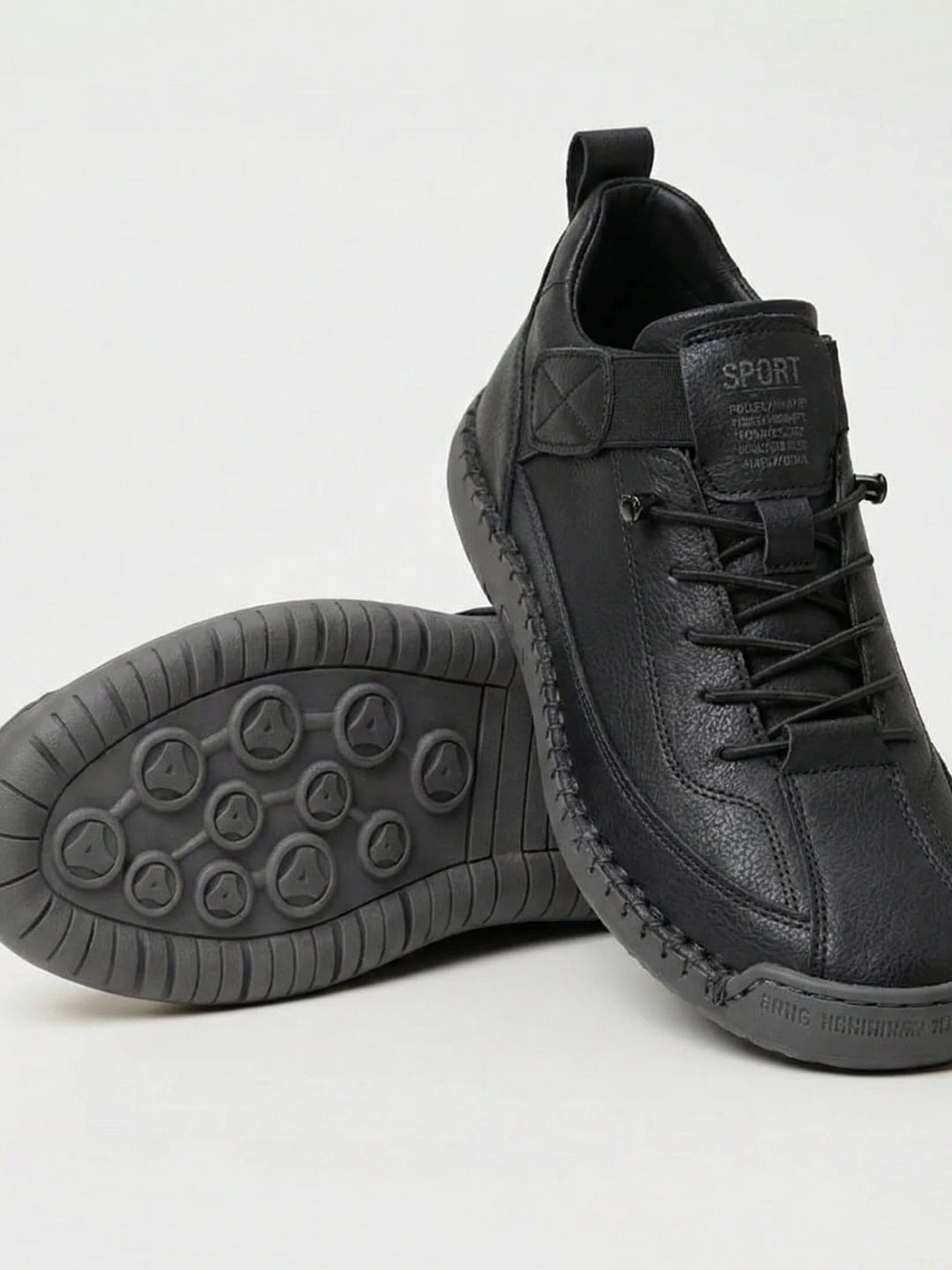 Czarne sneakersy ze skóropodobnej cholewki i szarą podeszwą z wzorem, jeden but oparty na drugim 1