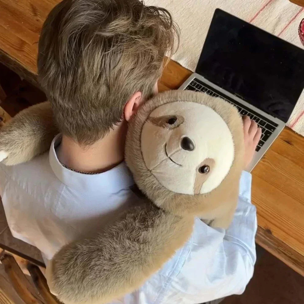 Widok z góry na mężczyznę przy laptopie, któremu pluszowy leniwiec oplata ramionami szyję i bark. 9