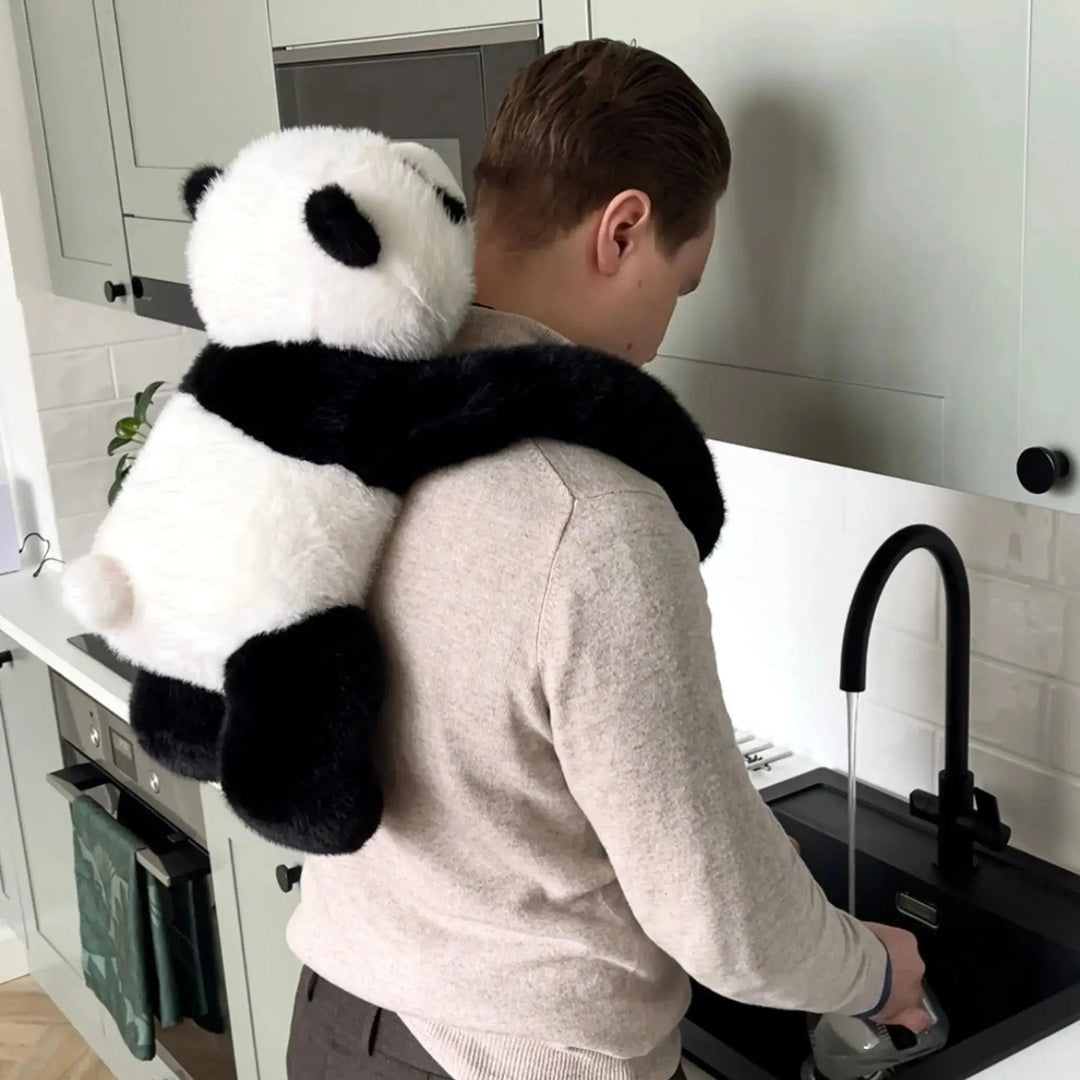 Mężczyzna zmywa naczynia przy zlewie w kuchni, a pluszowa panda wisi mu na plecach, obejmując ramionami szyję. 10