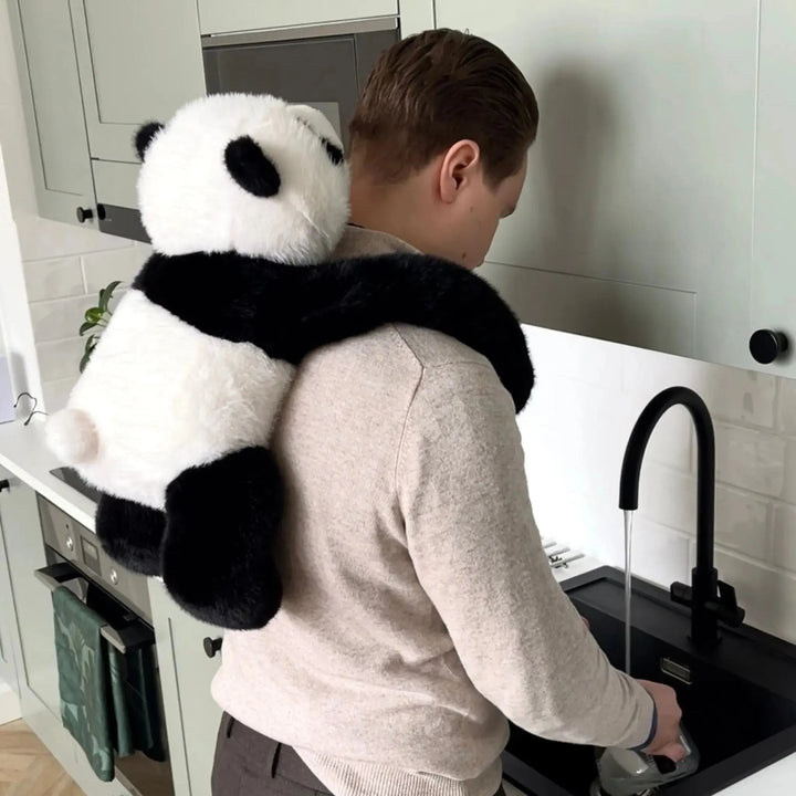 Mężczyzna zmywa naczynia przy zlewie w kuchni, a pluszowa panda wisi mu na plecach, obejmując ramionami szyję. 10