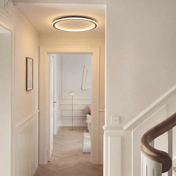 Lampa sufitowa świeci w korytarzu z białymi listwami, parkietem w jodełkę i schodami z drewnianą poręczą. 5