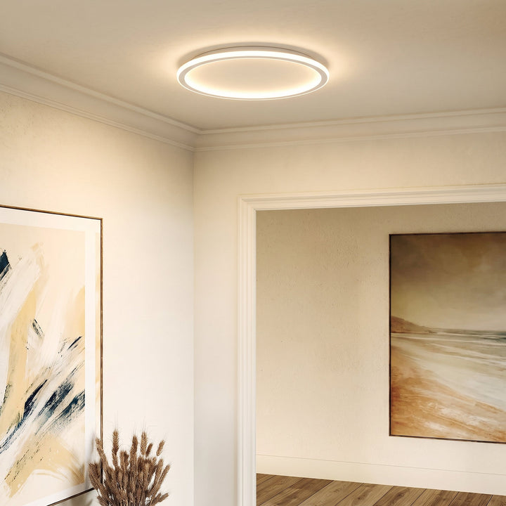 Lampa pierścieniowa na suficie w jasnym korytarzu ze sztukaterią, obok obrazy i wazon z suszonymi kłosami. 3
