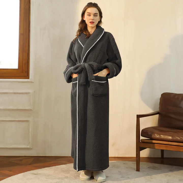 Modelka w grafitowym szlafroku z białym wykończeniem, ręce w kieszeniach, obok brązowy skórzany fotel 2
