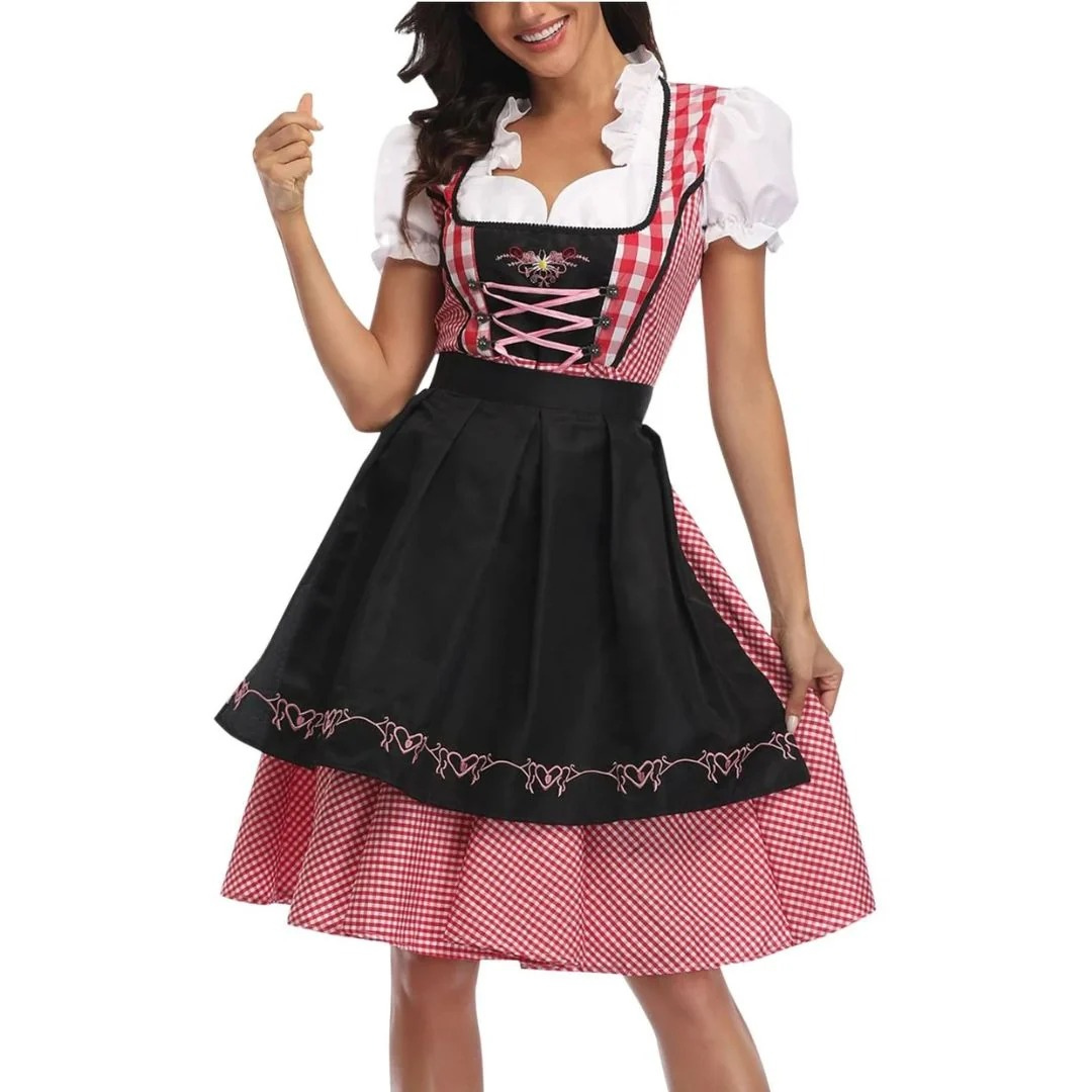 Modelka w czerwono-białej sukience dirndl z czarnym fartuchem z haftowanymi sercami, różowym sznurowaniem gorsetu i bufiastymi rękawkami, widok z przodu. 1