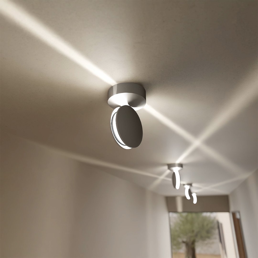 Biała lampa sufitowa z obróconą głowicą rzuca na sufit skośne, krzyżujące się wiązki światła, w tle kolejne lampy. 4
