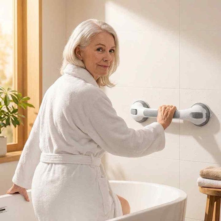 Starsza kobieta w białym szlafroku trzyma się biało-szarego uchwytu z przyssawkami na płytkach nad wanną. 1